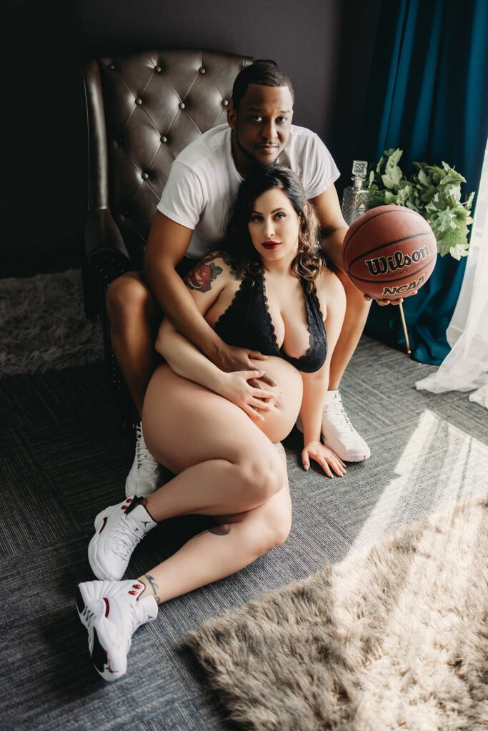 An interracial couple doing a maternity photoshoot indoors, using a basketball theme to show their love for the sport and their new baby that is yet to arrive