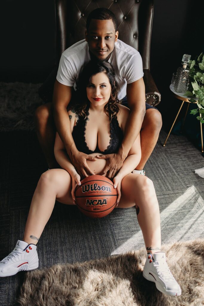 A couple doing an indoor maternity shoot, showing their excitement for their new baby with a basketball theme for their family photo session