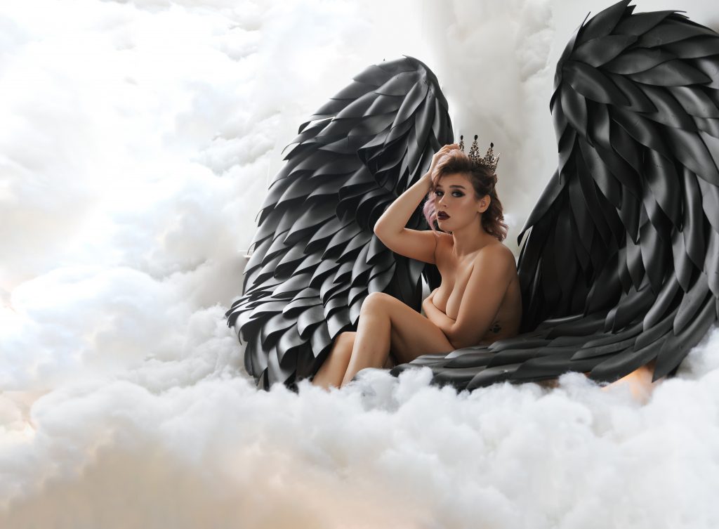 woman posing against fluffy cloud background wearing black angel wings and crown looking into camera and wearing red lipstick and queens crown Dijana Szewczyk photography Portland Oregon Boudoir Washington