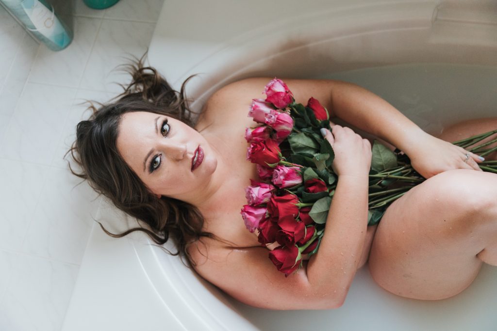 beautiful Caucasian brunette holding pink and red roses against chest in milky water for bath set red lipstick Dijana Szewczyk photography Portland Oregon Boudoir Washington