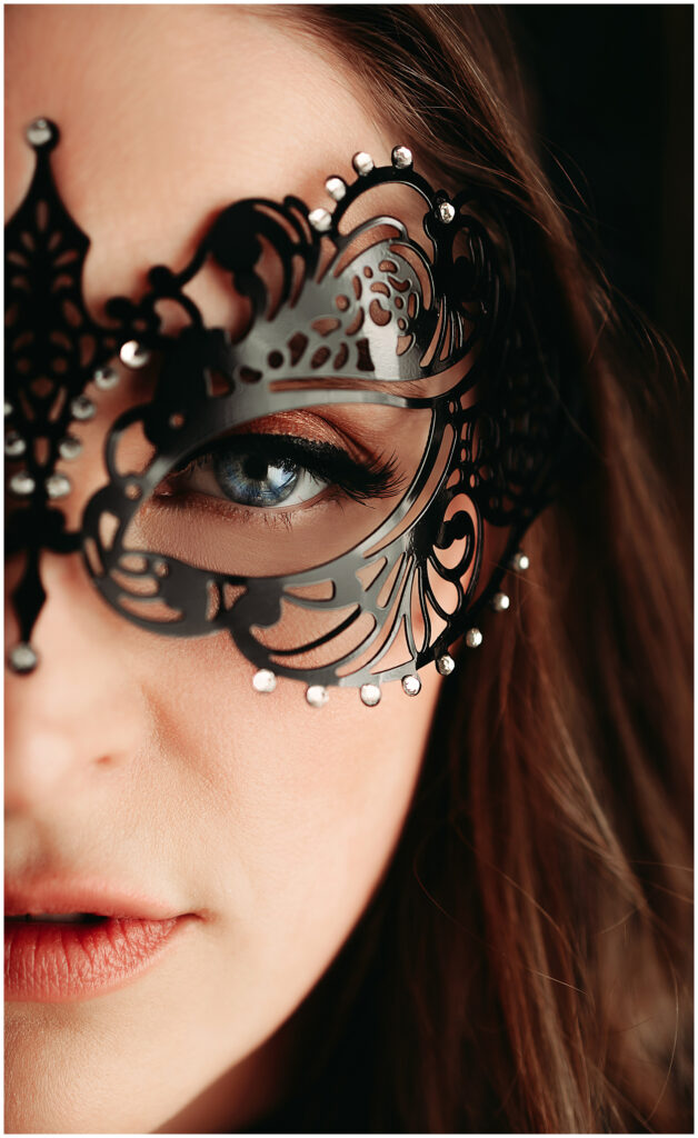 a close up of a woman wearing a masquerade mask, you can only see the left side of her face. she has brown hair and blue eyes and naturally colored lips.